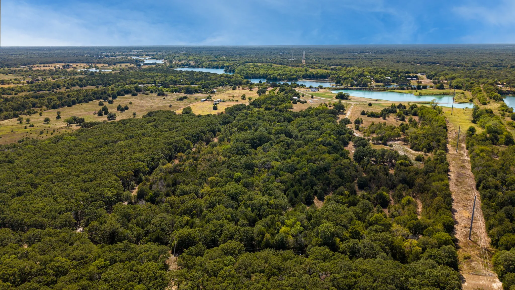 Expansive wooded acreage with a cleared pathway, bordered by a waterway and open land