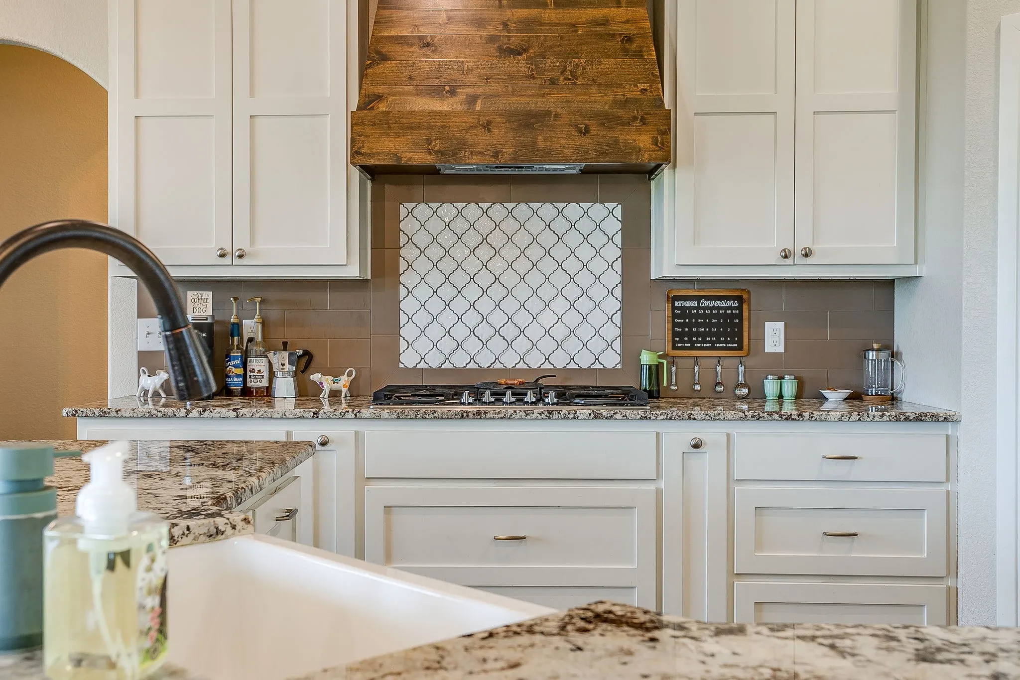 White shaker-style cabinetry with dark hardware, granite countertops, a built-in gas range, and a wood-finish range hood