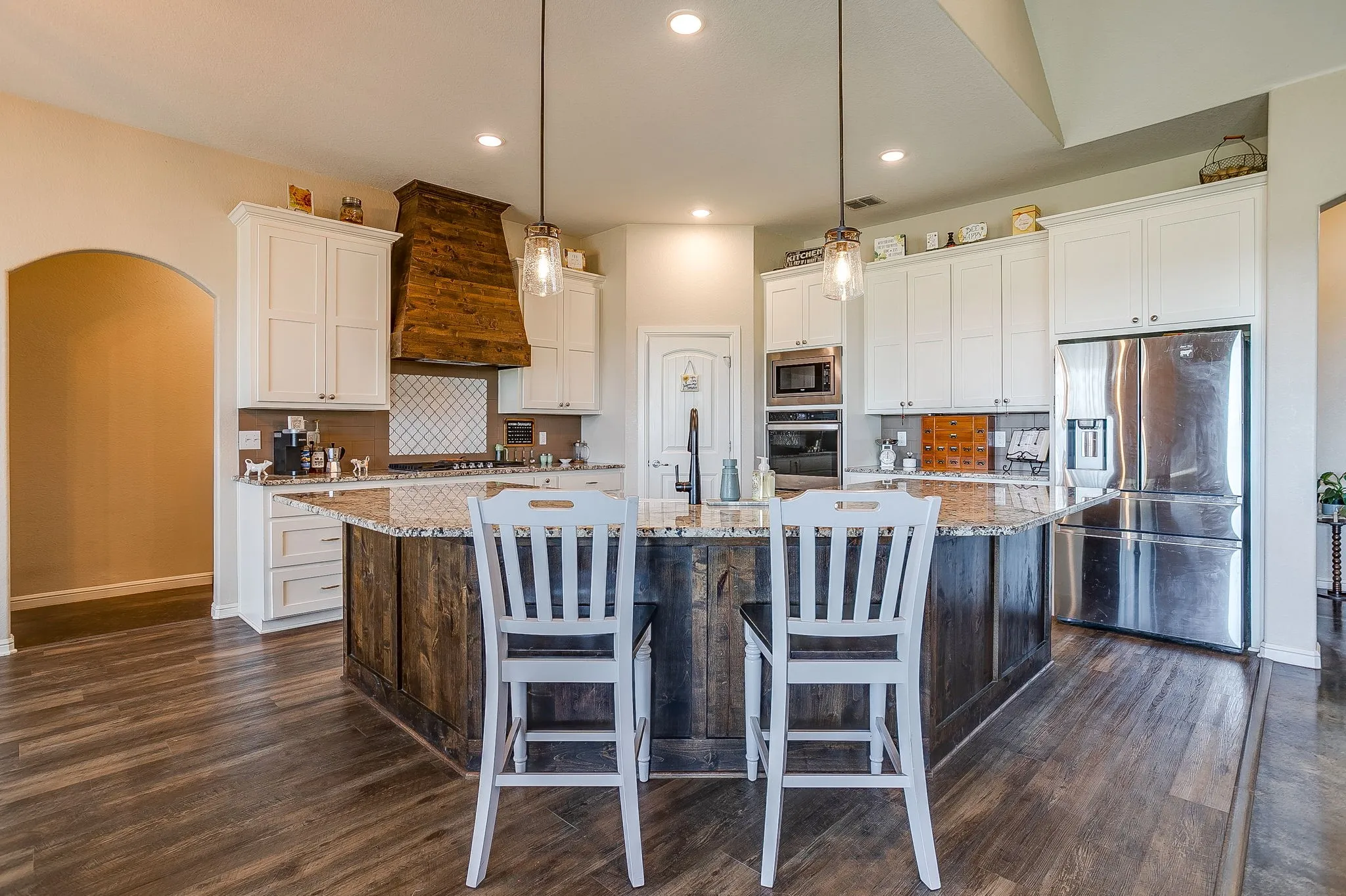 Kitchen featuring a wood-finish flooring, white cabinetry, a wood-paneled range hood, stainless steel appliances, and an island with a stone countertop