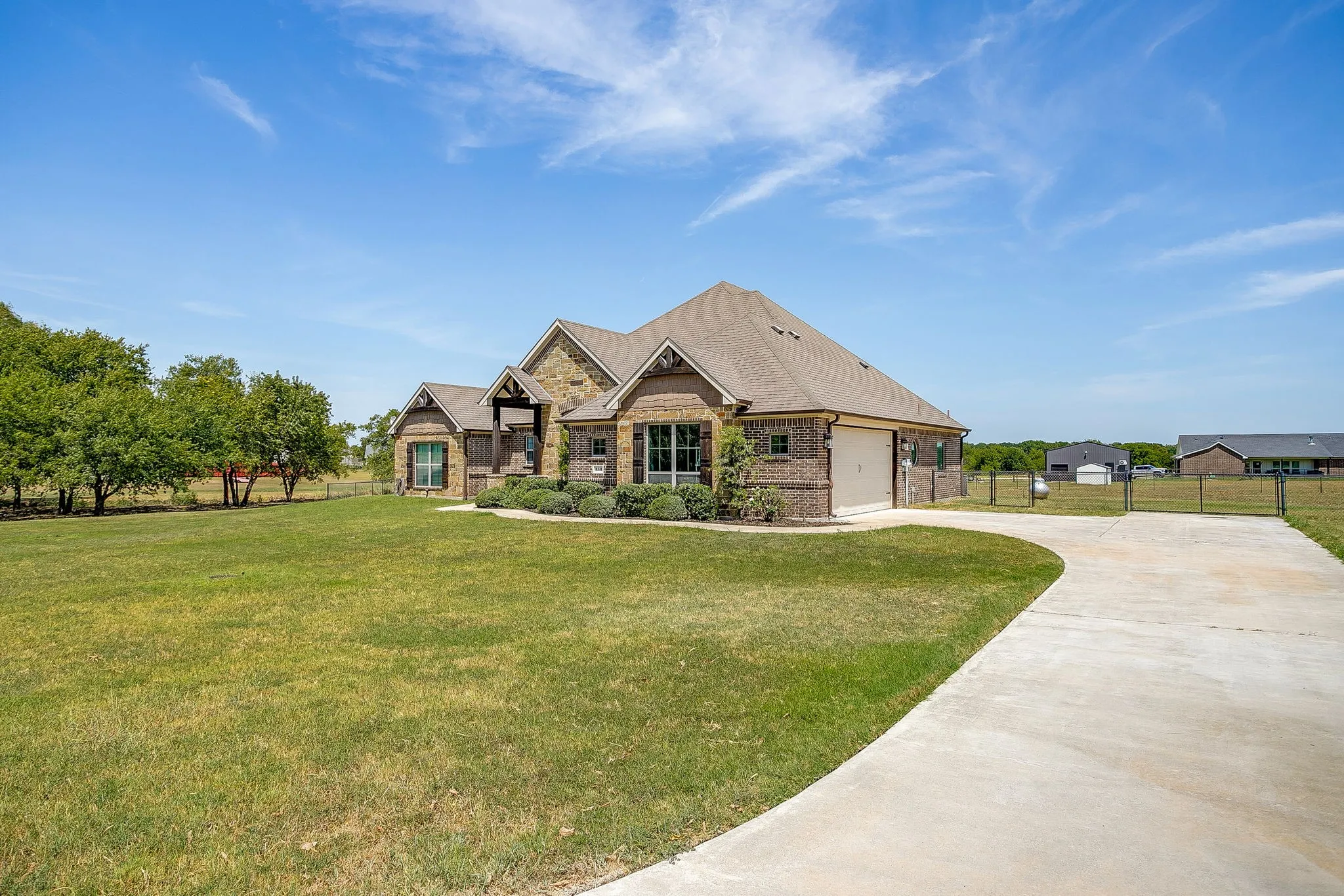 Exterior featuring a brick and stone facade, gabled roofline, attached garage, and a concrete​​‌​​​​‌​​‌‌​‌‌​​​‌‌​‌​‌​‌​​​‌​​ driveway