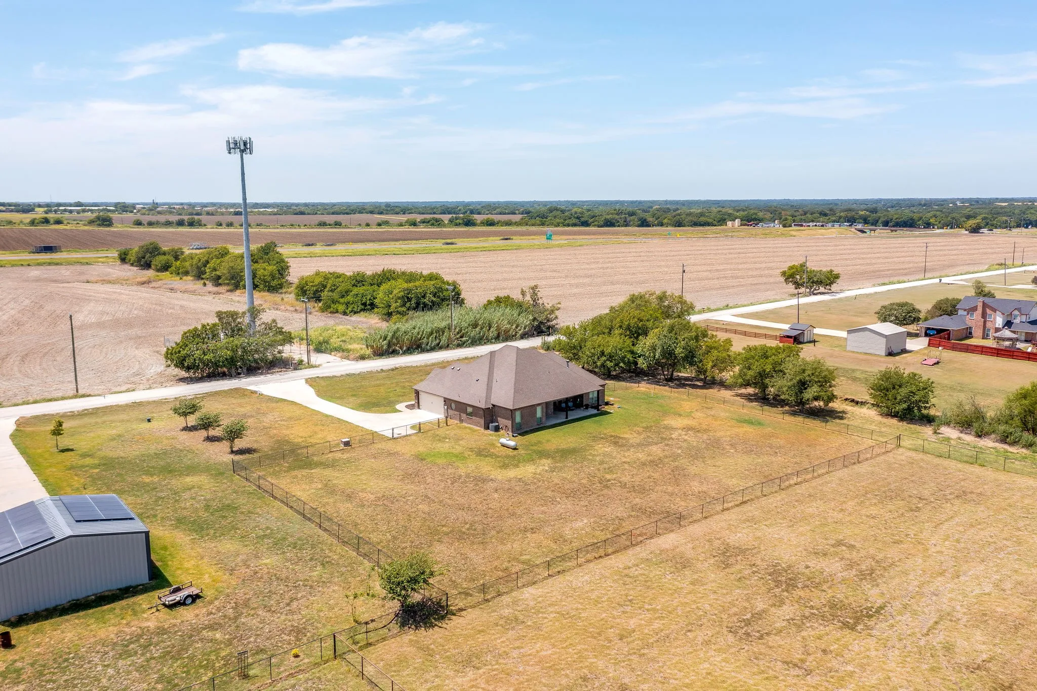 Extensive acreage featuring a single-story residence with an attached garage, a detached building with solar panels, and a fenced perimeter