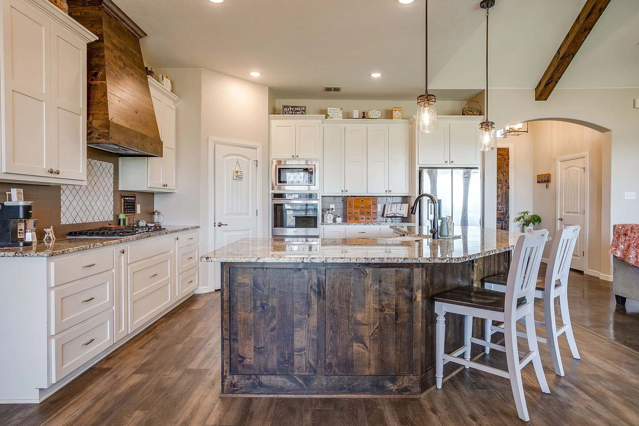 Kitchen featuring a large central island, white cabinetry, a wood-finish range hood, stainless steel appliances, and wood-finish flooring