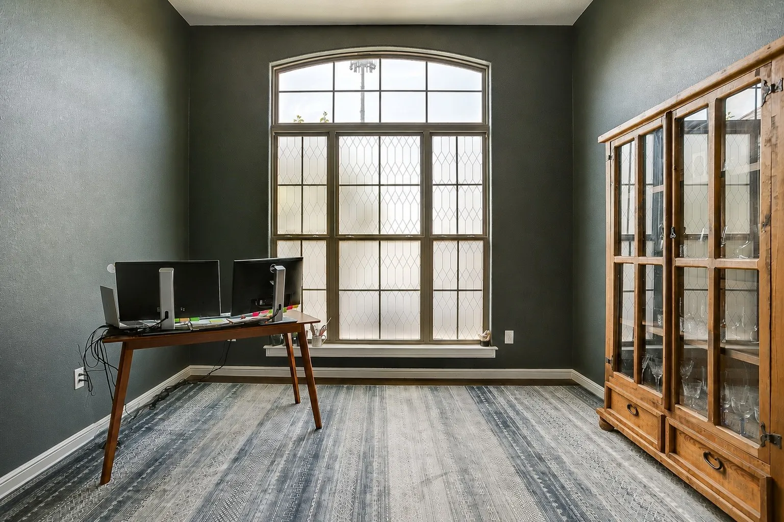 Arch-top window with decorative mullions, dark wall finishes, and wood-finish flooring - image slightly altered with AI