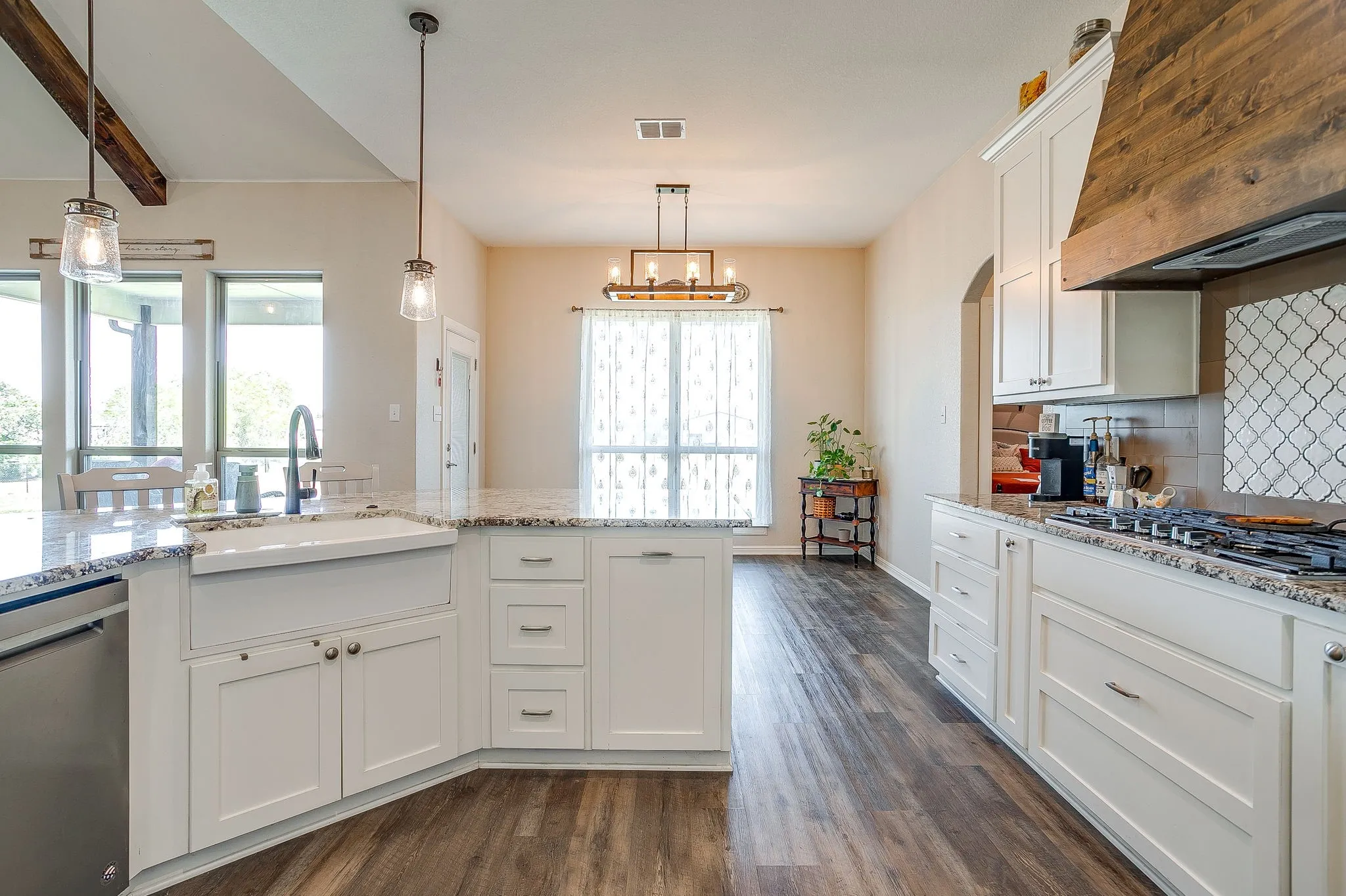 White cabinetry, granite countertops, wood-finish flooring, exposed wood beam, and a built-in gas range