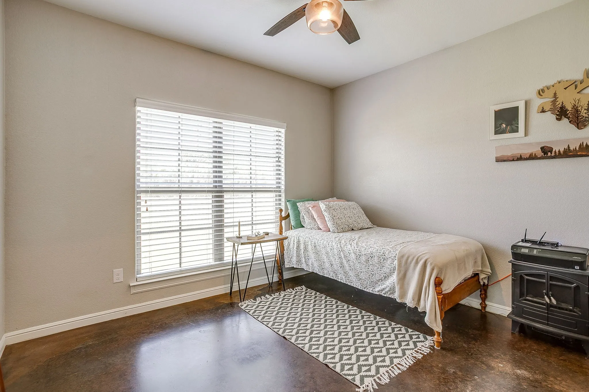 Expansive room with dark polished concrete flooring, neutral wall tones, a large window with blinds, and a ceiling fan with integrated lighting