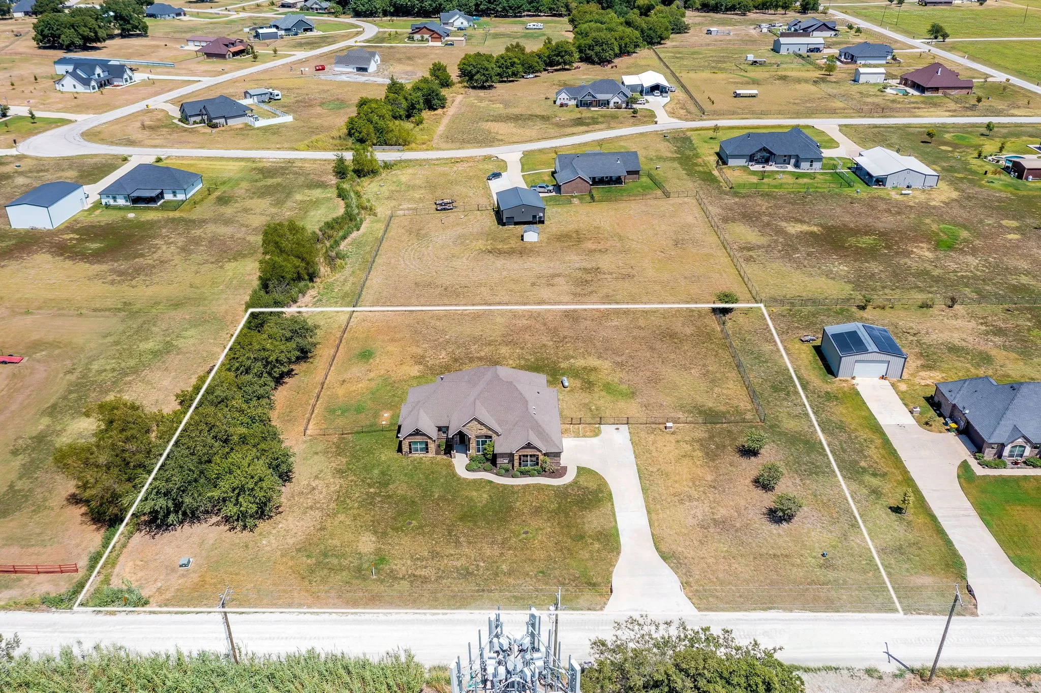 Aerial perspective showcasing a single-story residence with an attached garage, a defined concrete driveway, and a partially wooded property line