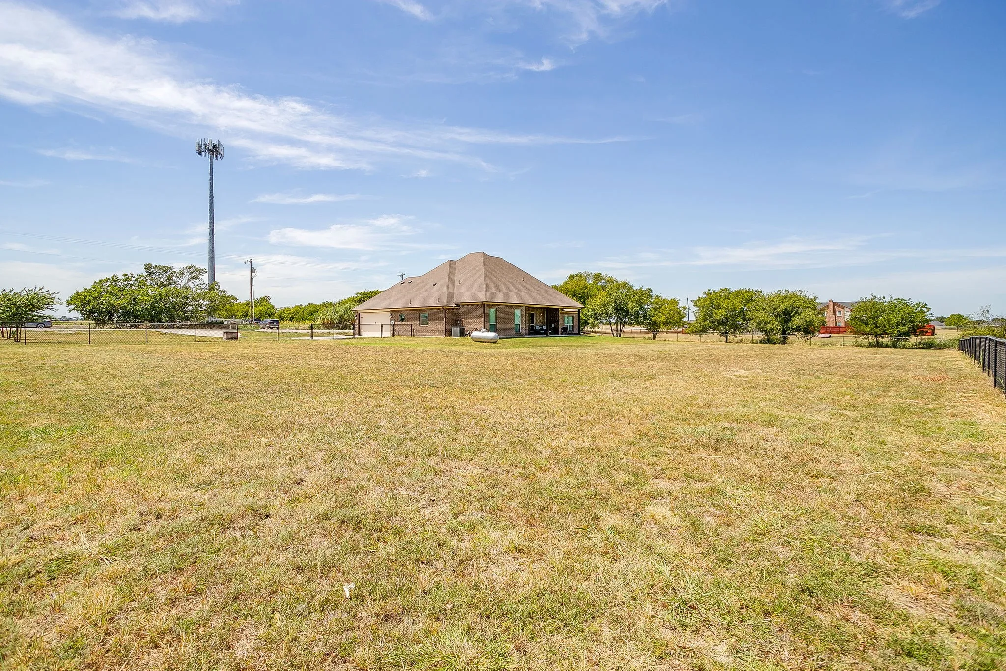 Expansive property featuring a brick exterior, shingled roof, covered patio, and metal fencing
