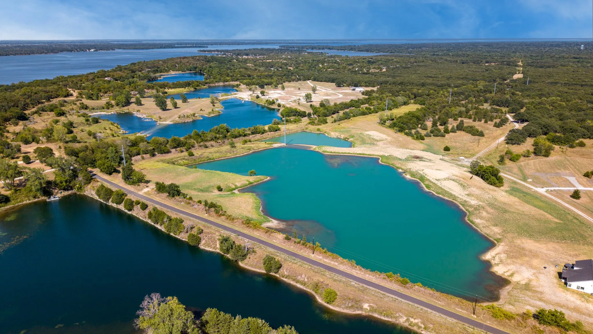 Expansive landscape featuring multiple bodies of water, extensive tree coverage, open land, and a single-story residence