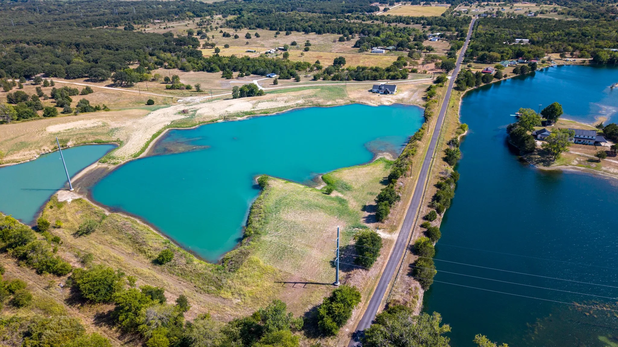 Expansive rural landscape featuring multiple bodies of water, diverse tree coverage, and an asphalt road