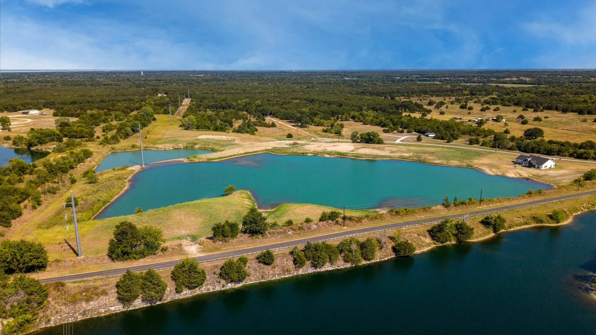 Expansive land parcel featuring multiple bodies of water, a paved road, and abundant mature trees