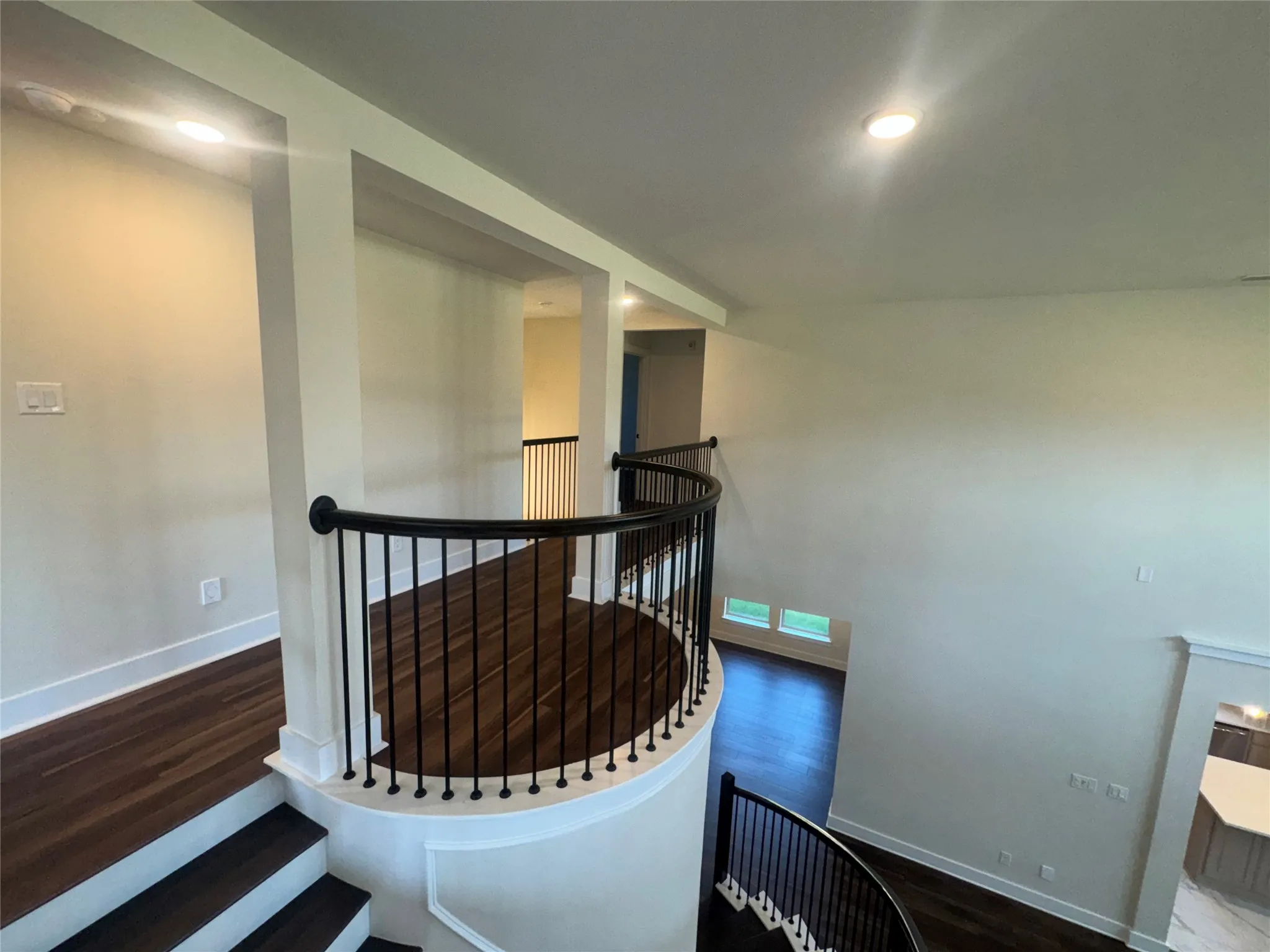 Curved staircase with black wrought iron balusters, wood-finish flooring, recessed lighting, and a neutral color palette