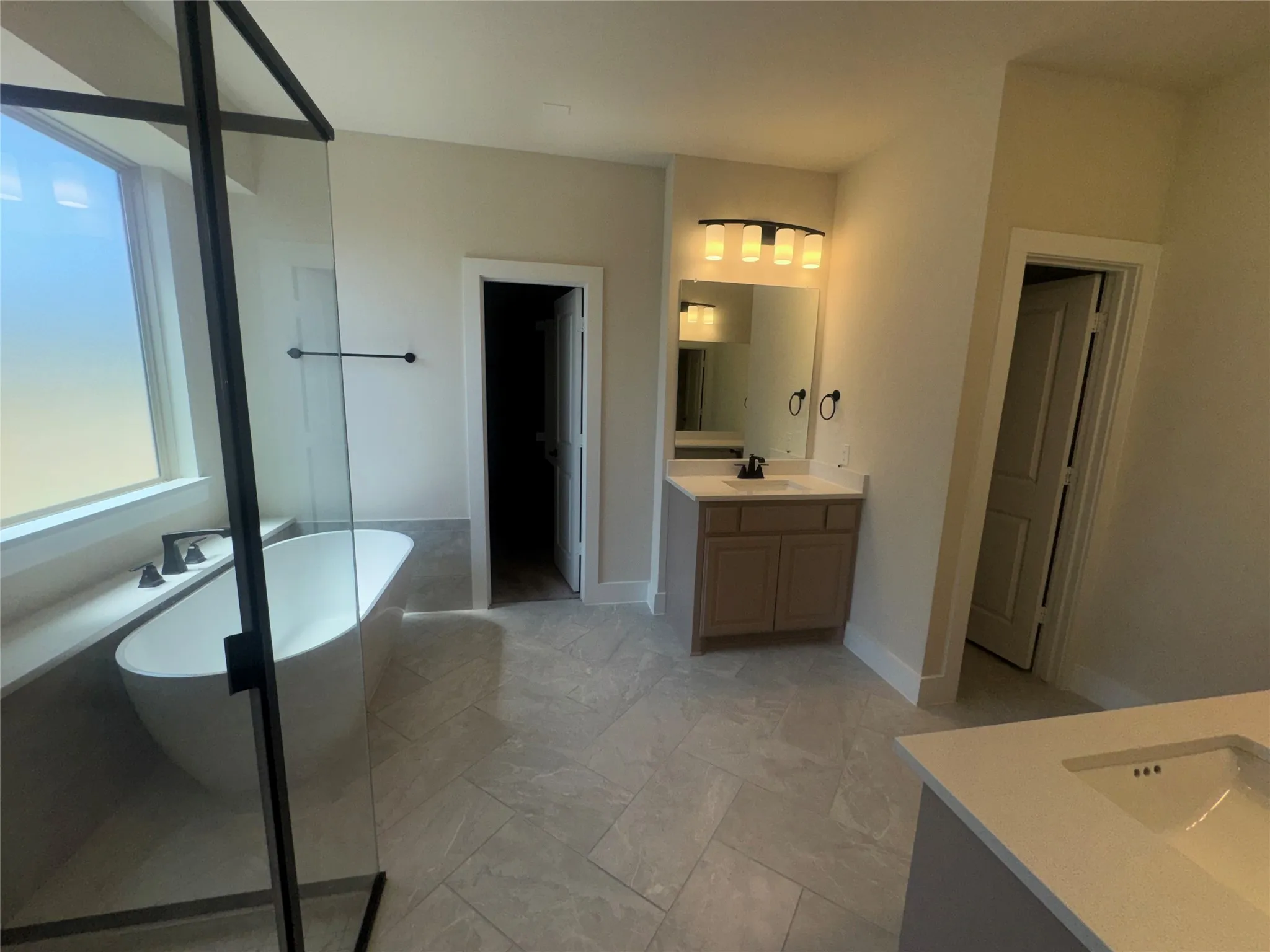 Freestanding soaking tub with matte black fixtures, glass-enclosed shower, dual vanity, and tiled flooring