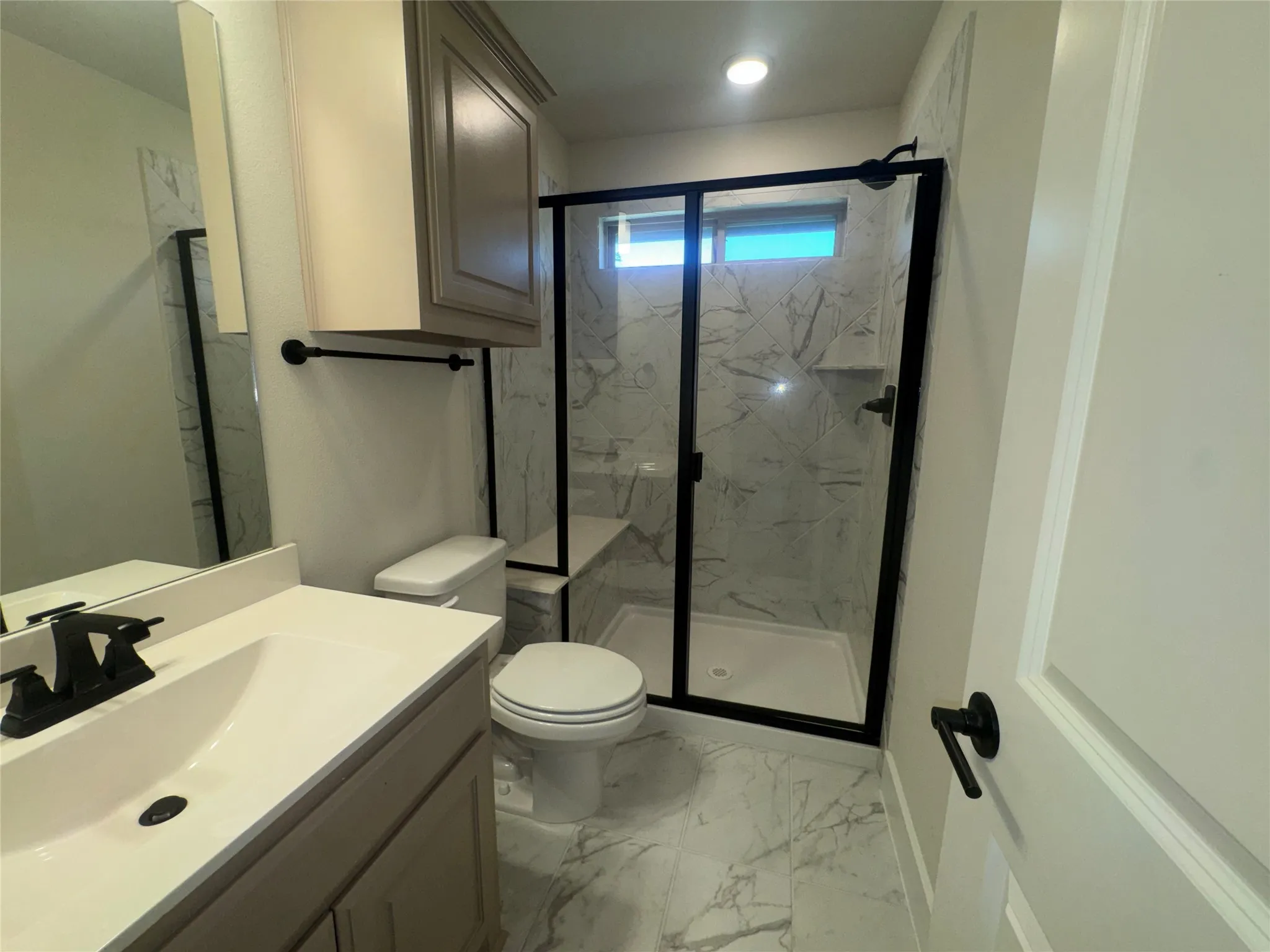 Walk-in shower with black-framed glass enclosure, integrated bench, and marble-patterned tile surround