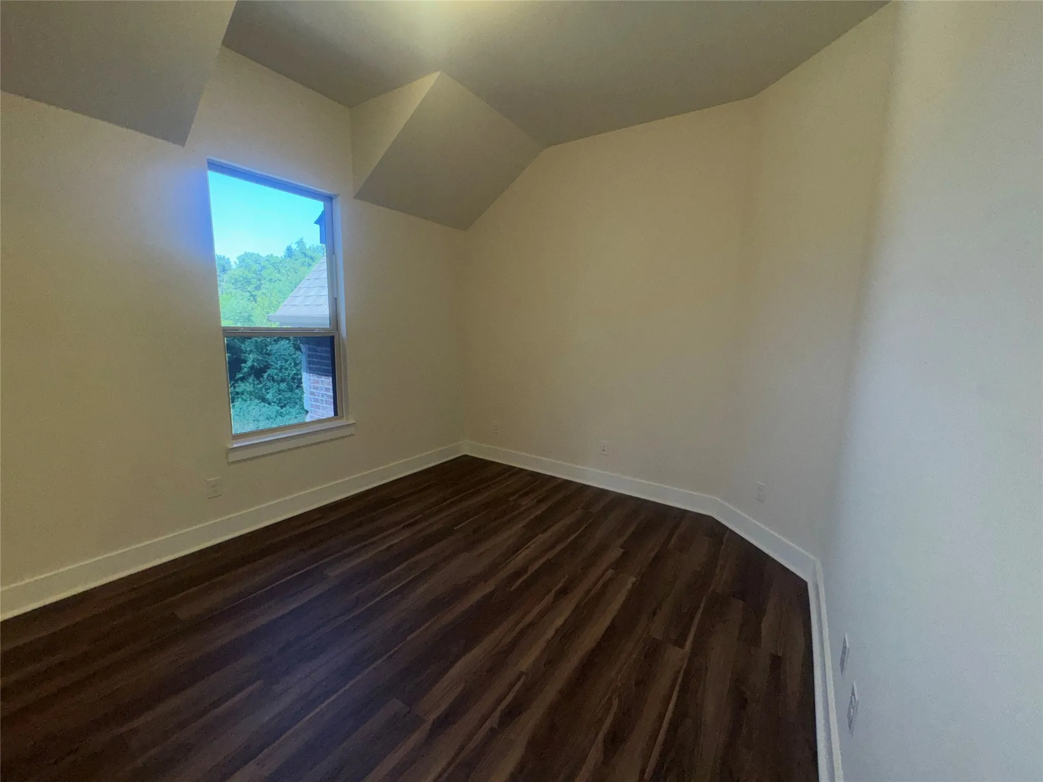 Light-filled room featuring sloped ceilings and wood-finish flooring