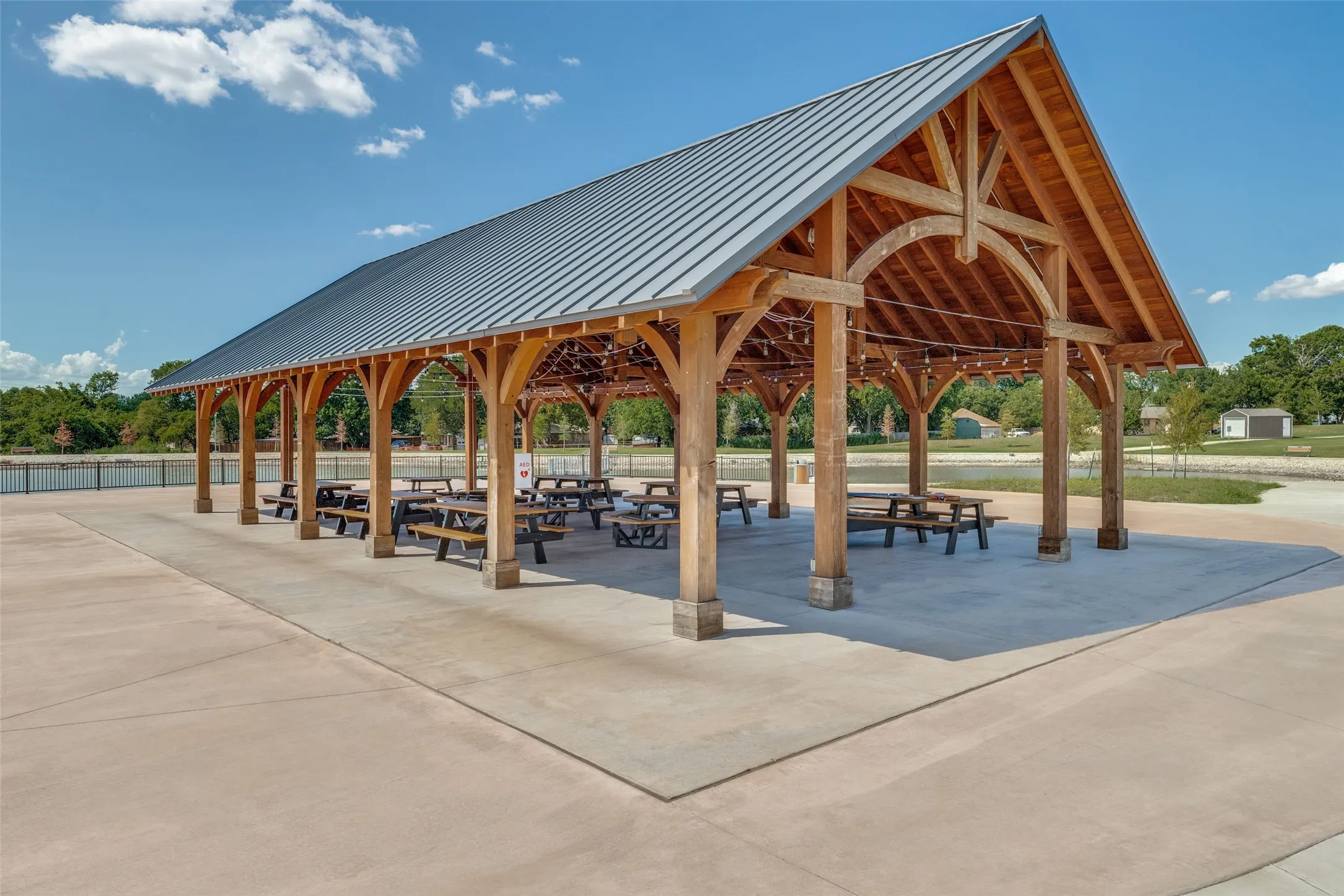 Expansive outdoor pavilion with a standing seam metal roof, exposed wood beam construction, and integrated string lighting
