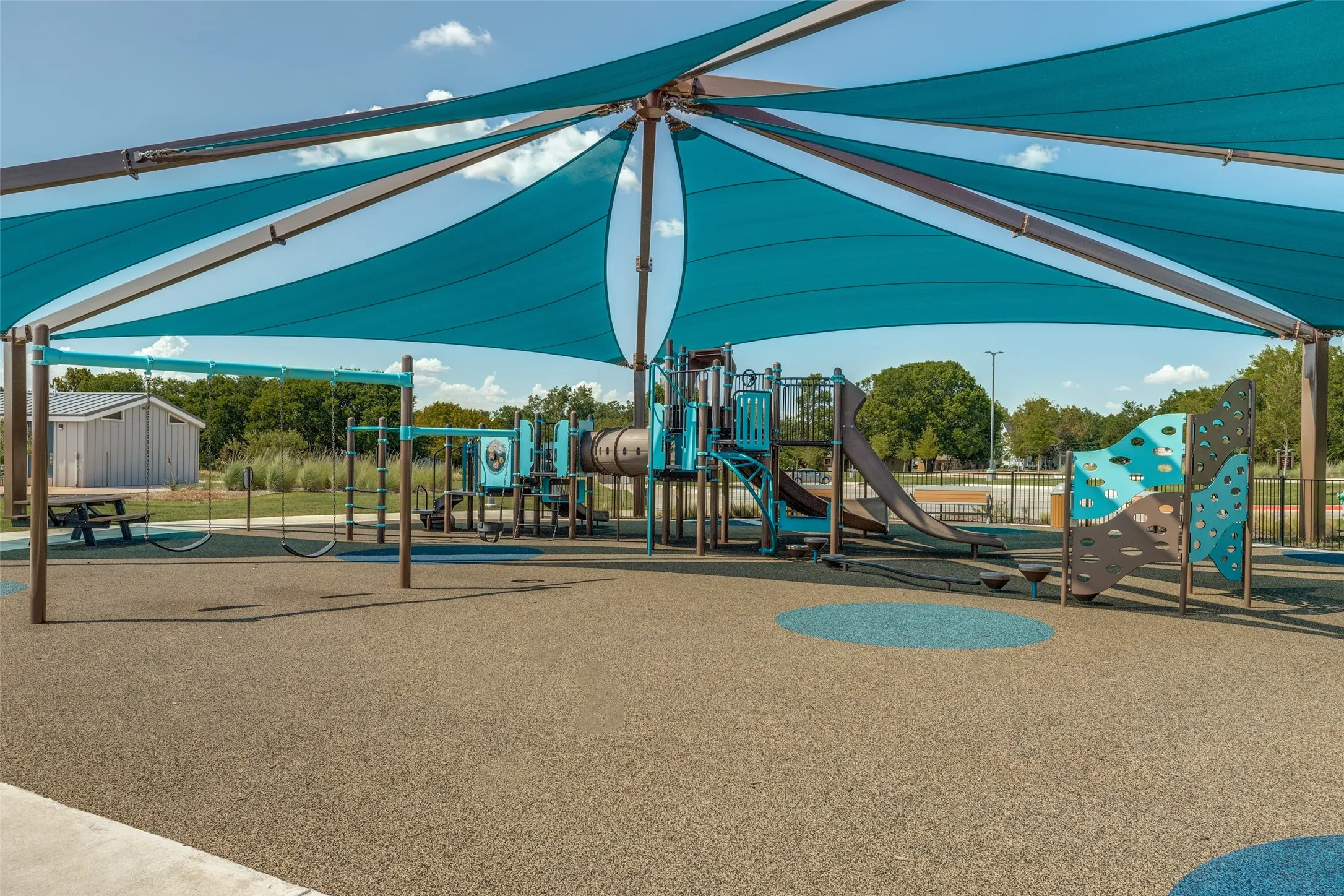 Playground with protective shade sails, padded ground surfacing, multiple slides, a climbing wall, and swing sets