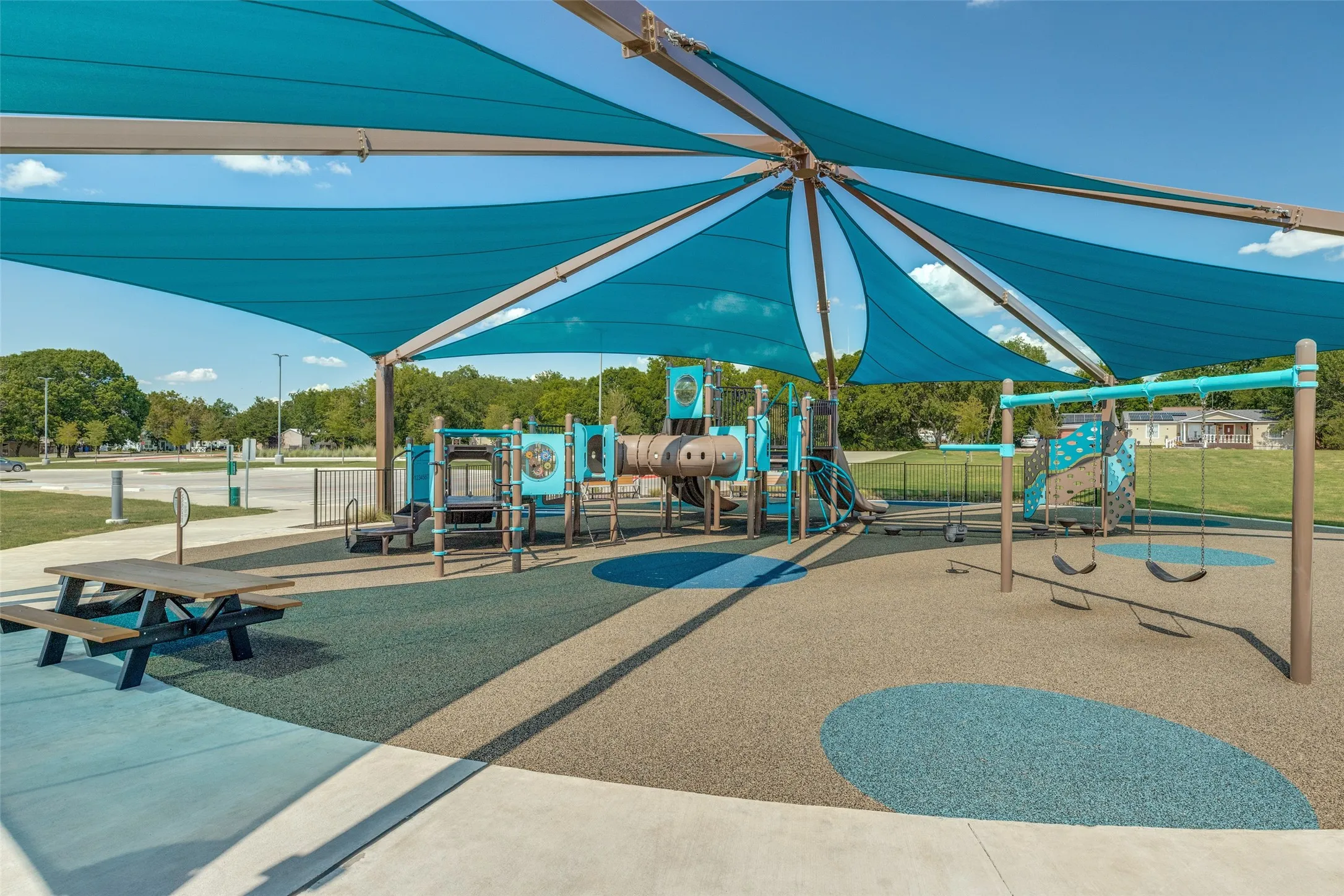 Playground area featuring a large shade structure, multiple play structures, swings, and a picnic table