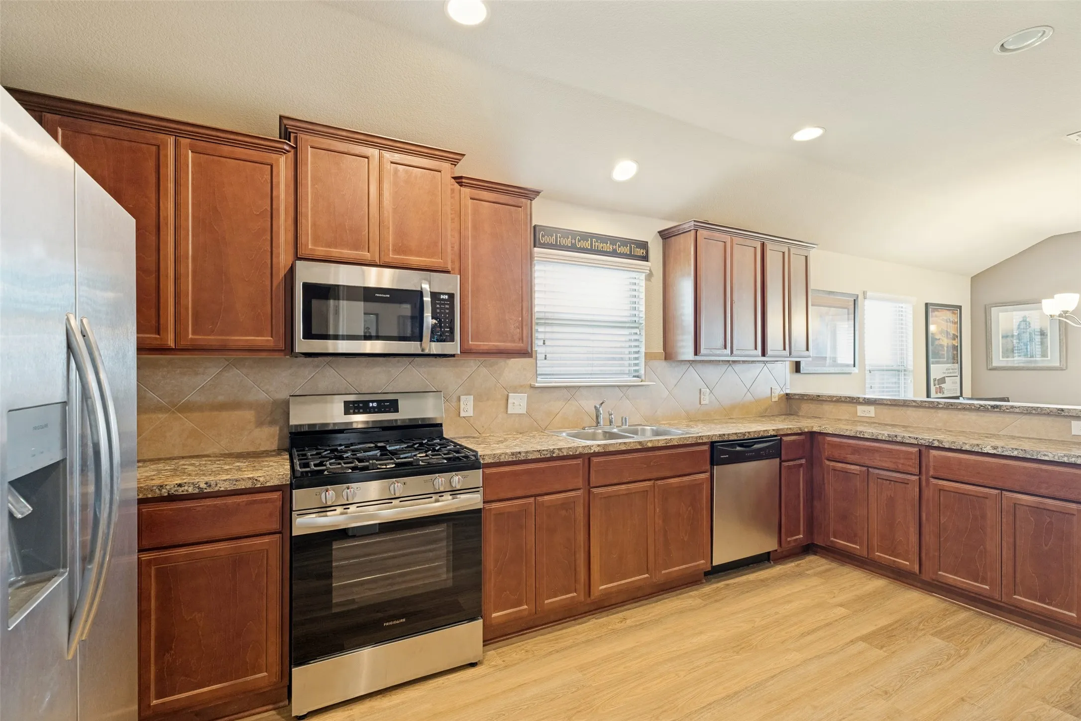 Kitchen featuring wood-finish flooring, stainless steel appliances, extensive cabinetry, a tile backsplash, and recessed lighting