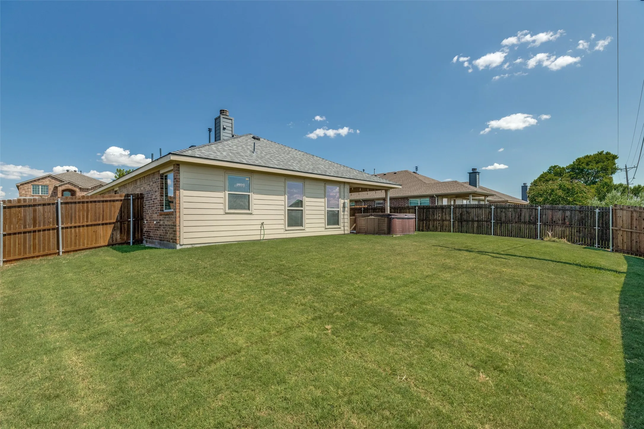Expansive green lawn with a hot tub, brick and siding exterior, and wood fencing
