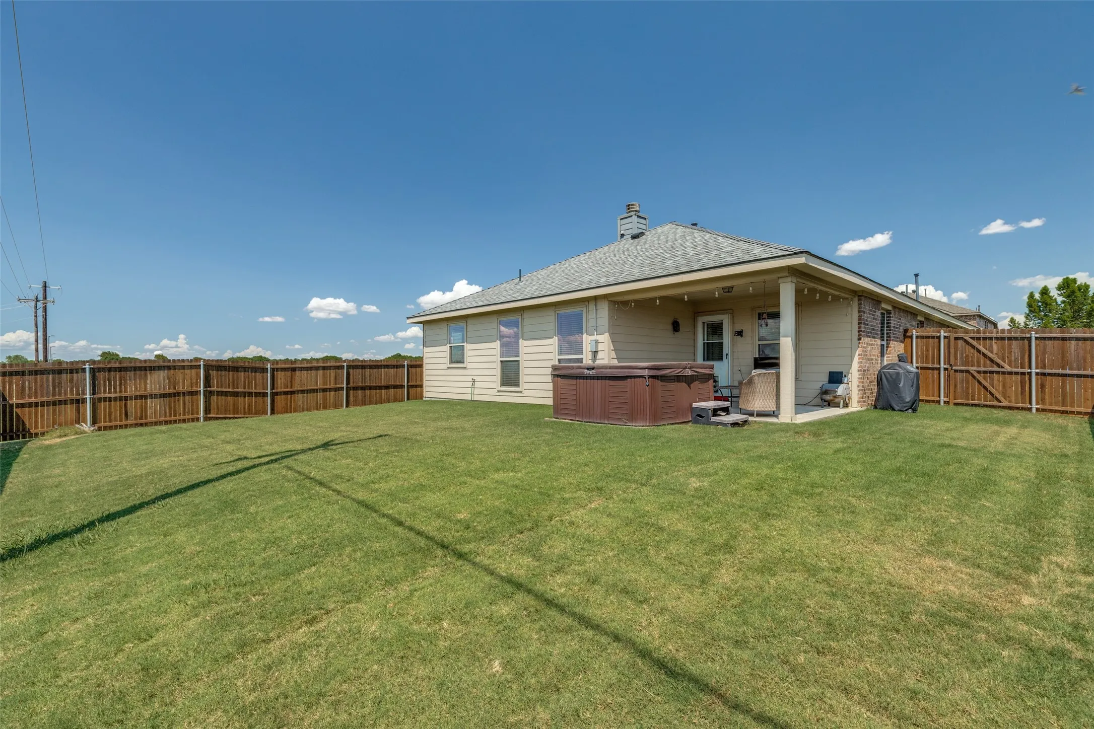 Expansive backyard featuring a covered patio, privacy fencing, and a built-in hot tub