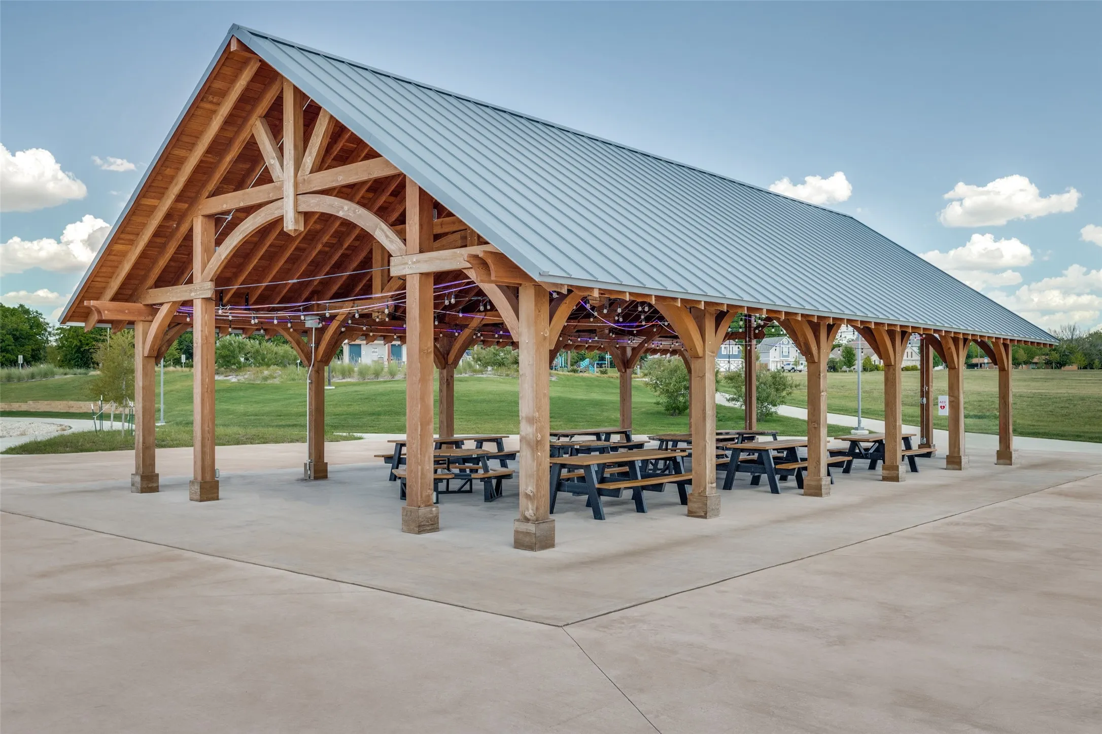 Expansive outdoor pavilion with a gabled metal roof, exposed wood beam construction, and concrete​​‌​​​​‌​​‌‌​‌‌​​​‌‌​‌​‌​‌​​​‌​​ flooring