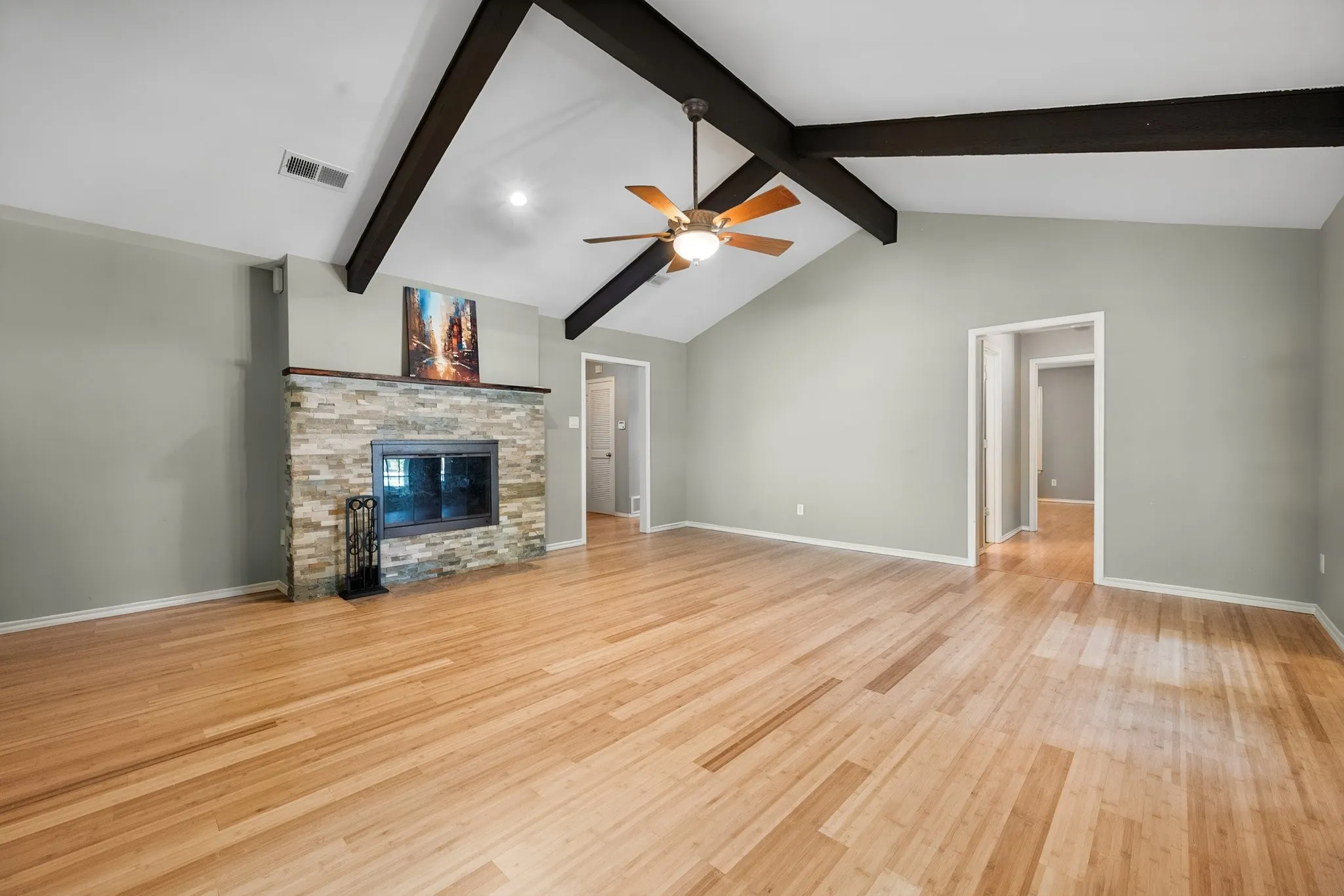 The spacious living room features bamboo flooring, a vaulted ceiling with exposed beams, and a stone-accented fireplace that anchors the room.
