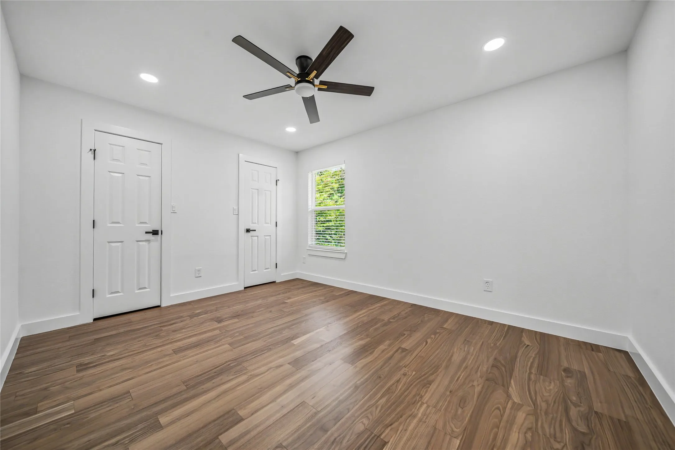 Spacious room featuring wood-finish flooring, white walls, and a modern ceiling fan with integrated lighting