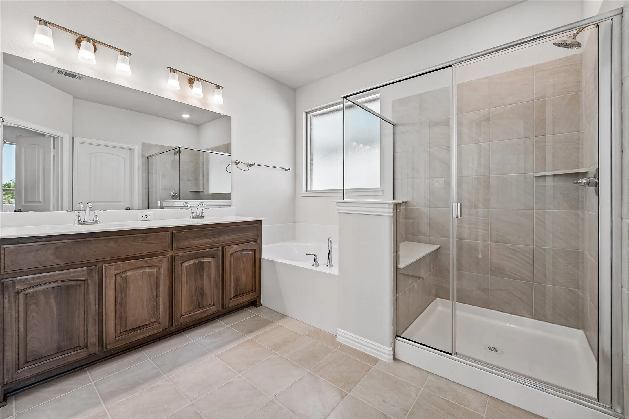 Spacious bathroom featuring a double vanity with ample cabinetry, a large soaking tub, and a separate glass-enclosed shower with tile surround