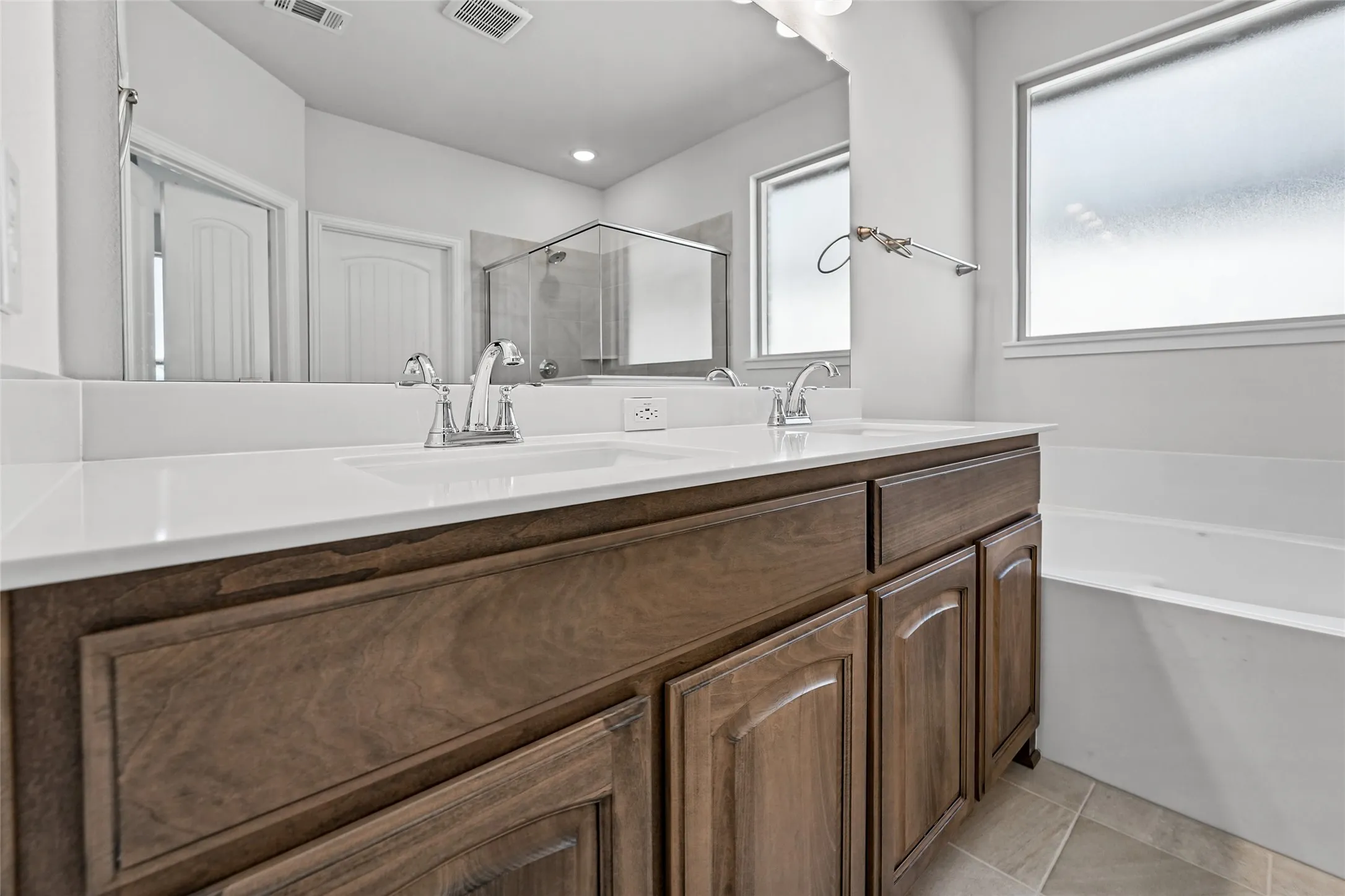 Spa-inspired primary bathroom featuring a dual-sink vanity with white quartz countertop, rich wood-finish cabinetry, and polished chrome fixtures