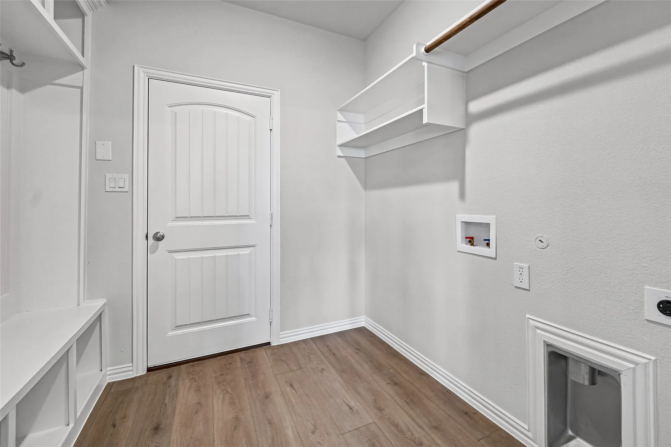 Laundry area featuring wood-finish flooring, built-in shelving, and a hanging rod