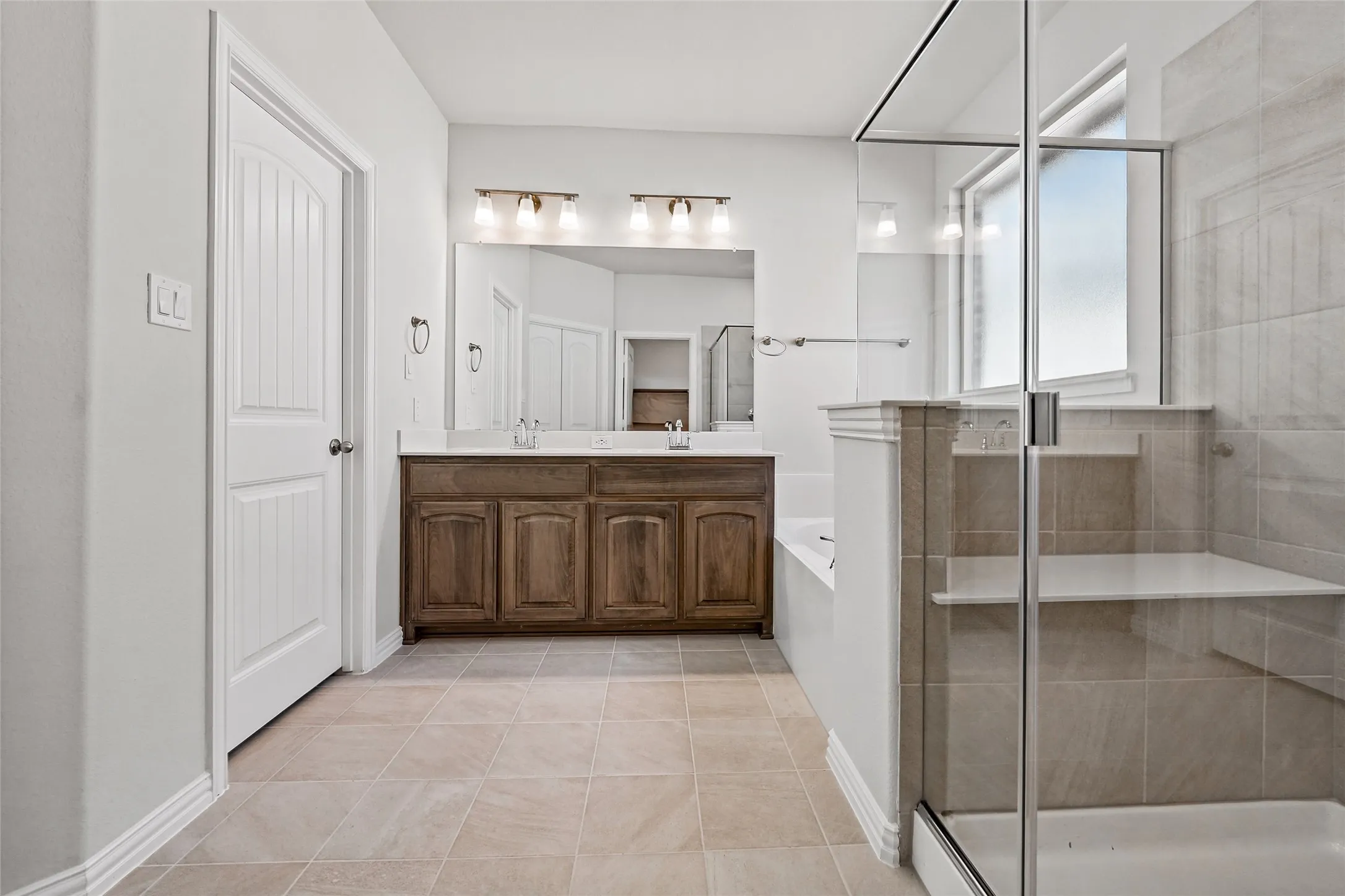 Spacious bathroom featuring a dual-sink wood-finish vanity, large framed mirror, built-in bathtub, and a glass-enclosed shower with integrated seating