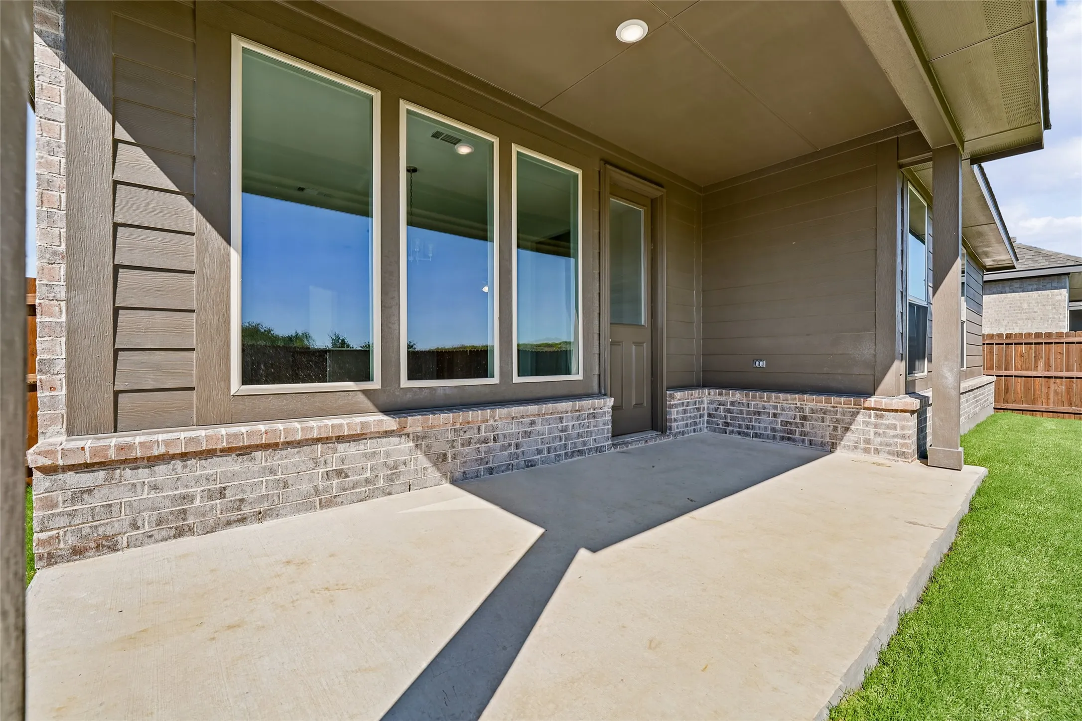 Covered concrete patio with brick and siding exterior, multiple windows, and a flush-mount overhead light