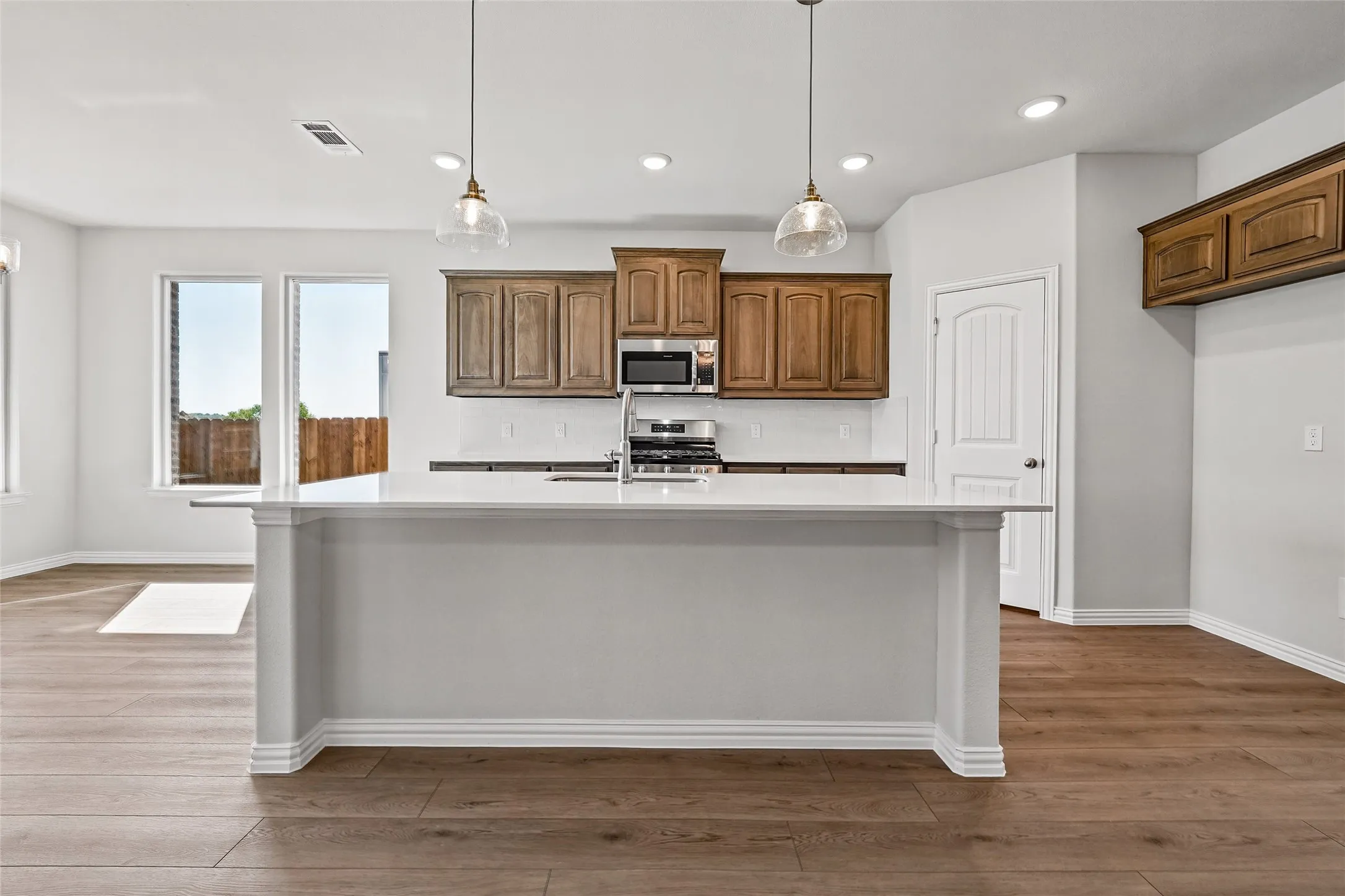 Kitchen featuring an island with a light-toned countertop, wood-finish flooring, recessed lighting, two pendant lights, and stainless steel appliances