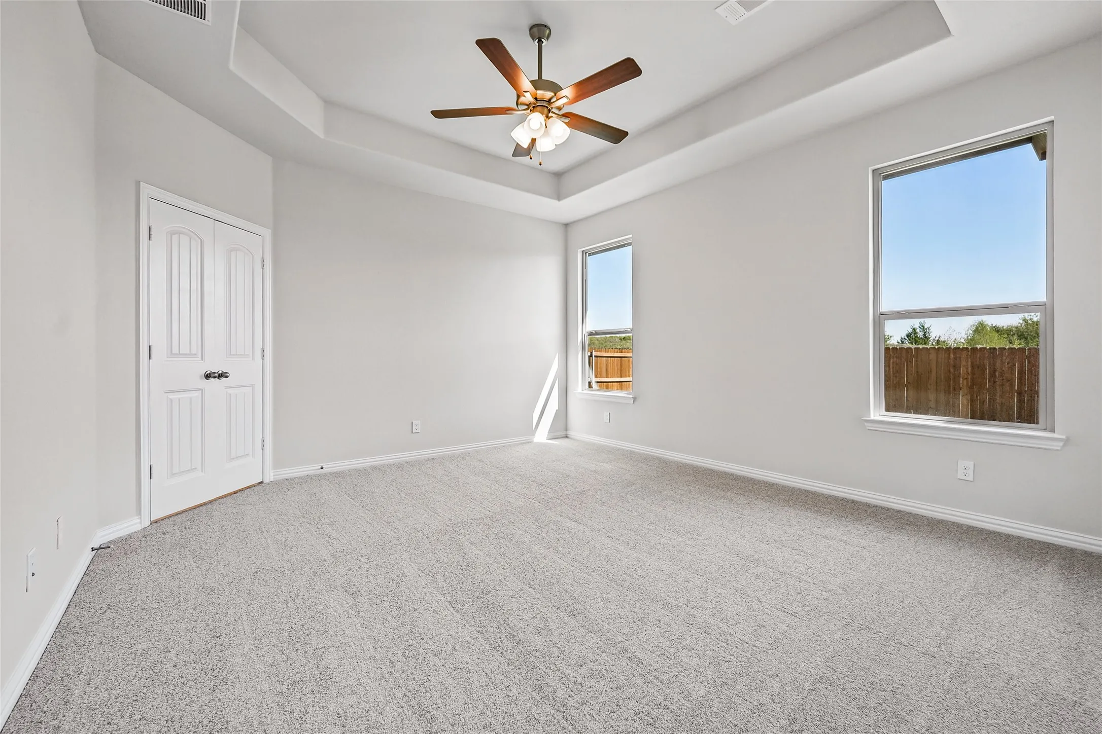 Tray ceiling with a ceiling fan light fixture, two windows, two-panel interior door, and carpet flooring