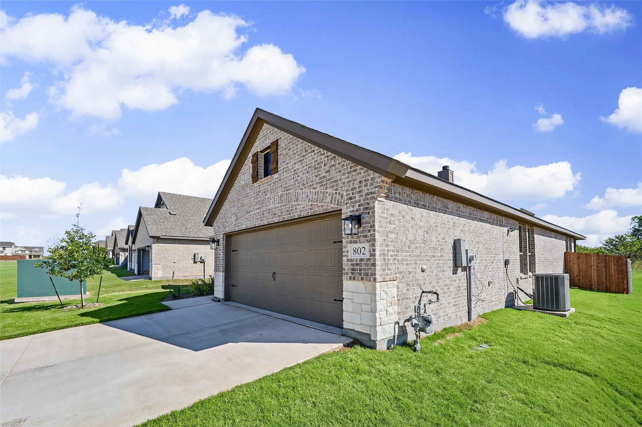 Brick exterior with stone accents, attached two-car garage, concrete driveway, and a wood privacy fence