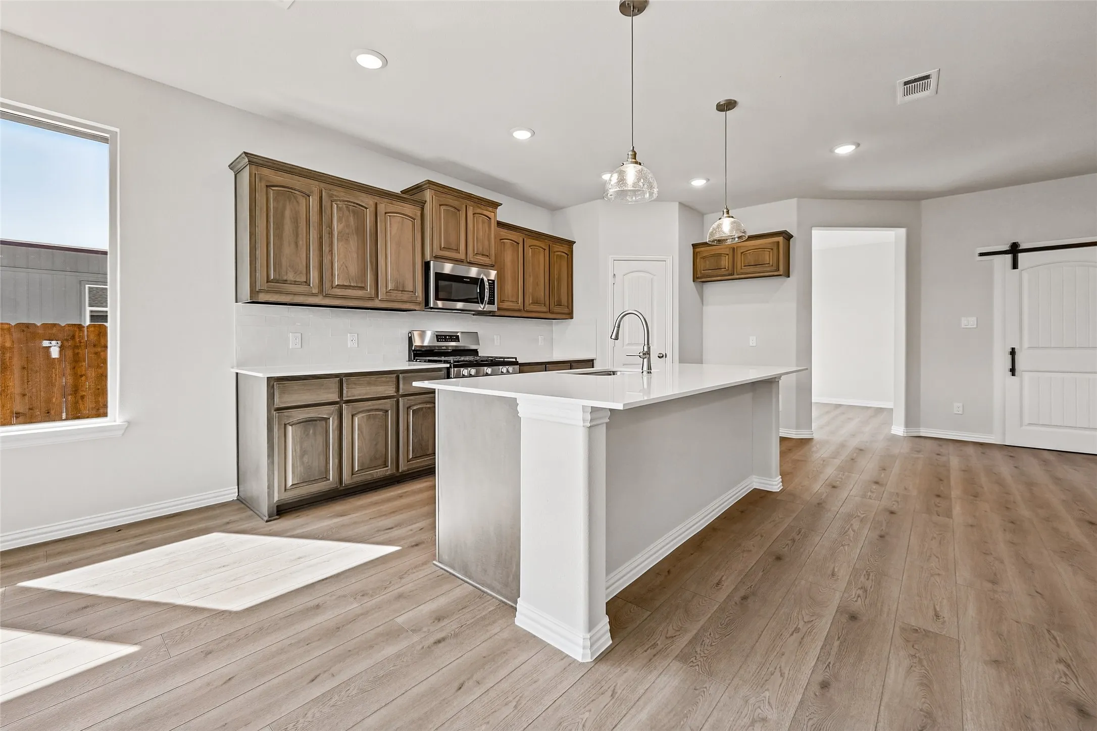 Open-concept kitchen with wood-finish flooring, custom wood cabinetry, stainless steel appliances, and a central island with a sink
