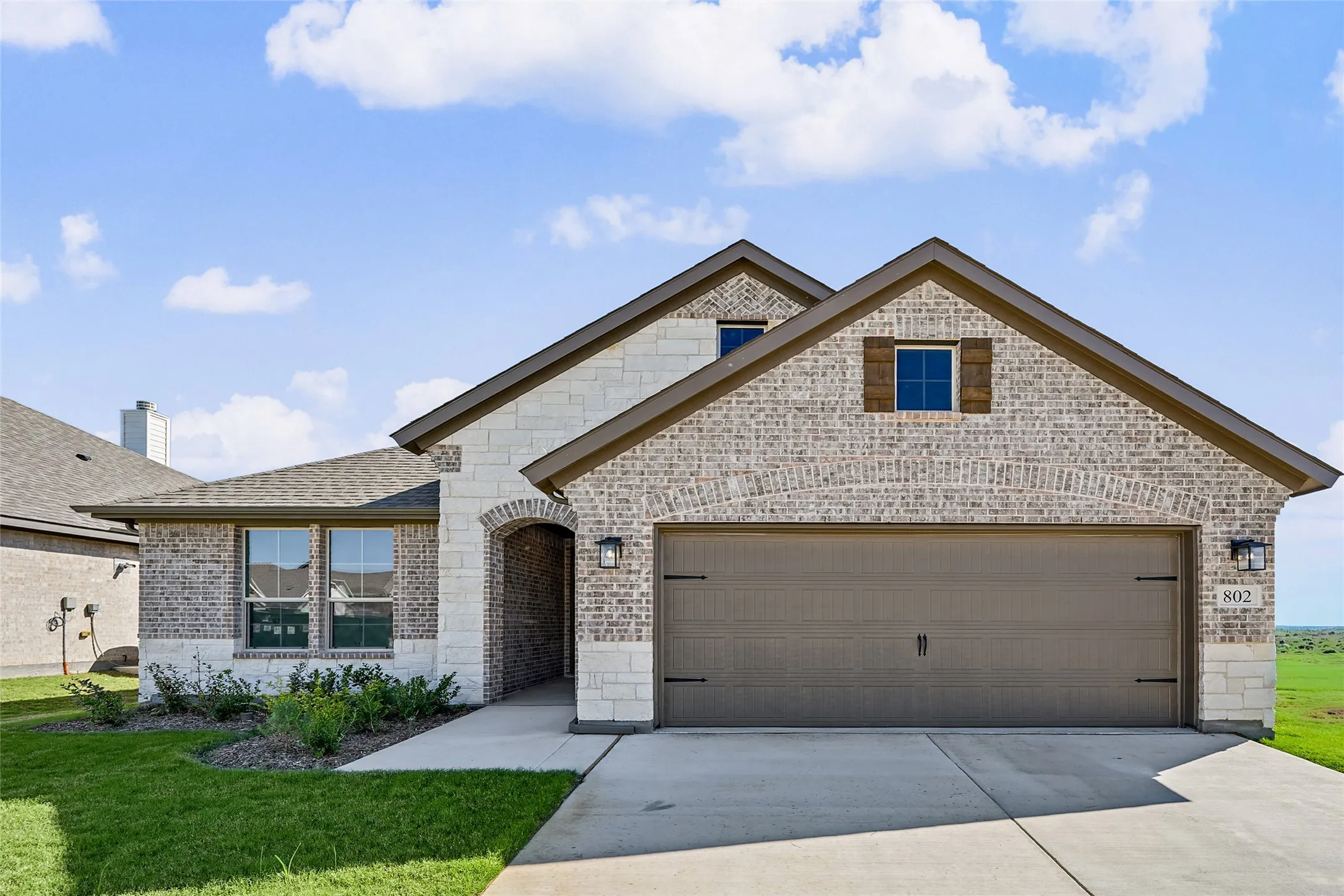 Brick and stone exterior with a two-car garage, arched entry, and decorative shutters