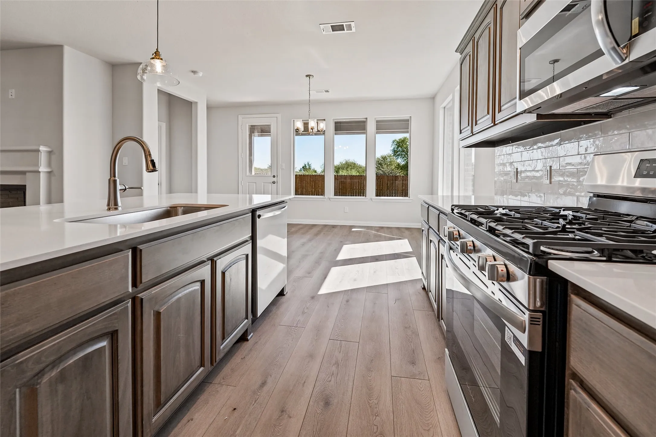 Gourmet kitchen featuring a gas range, stainless steel appliances, quartz countertops, a subway tile backsplash, and wood-finish flooring