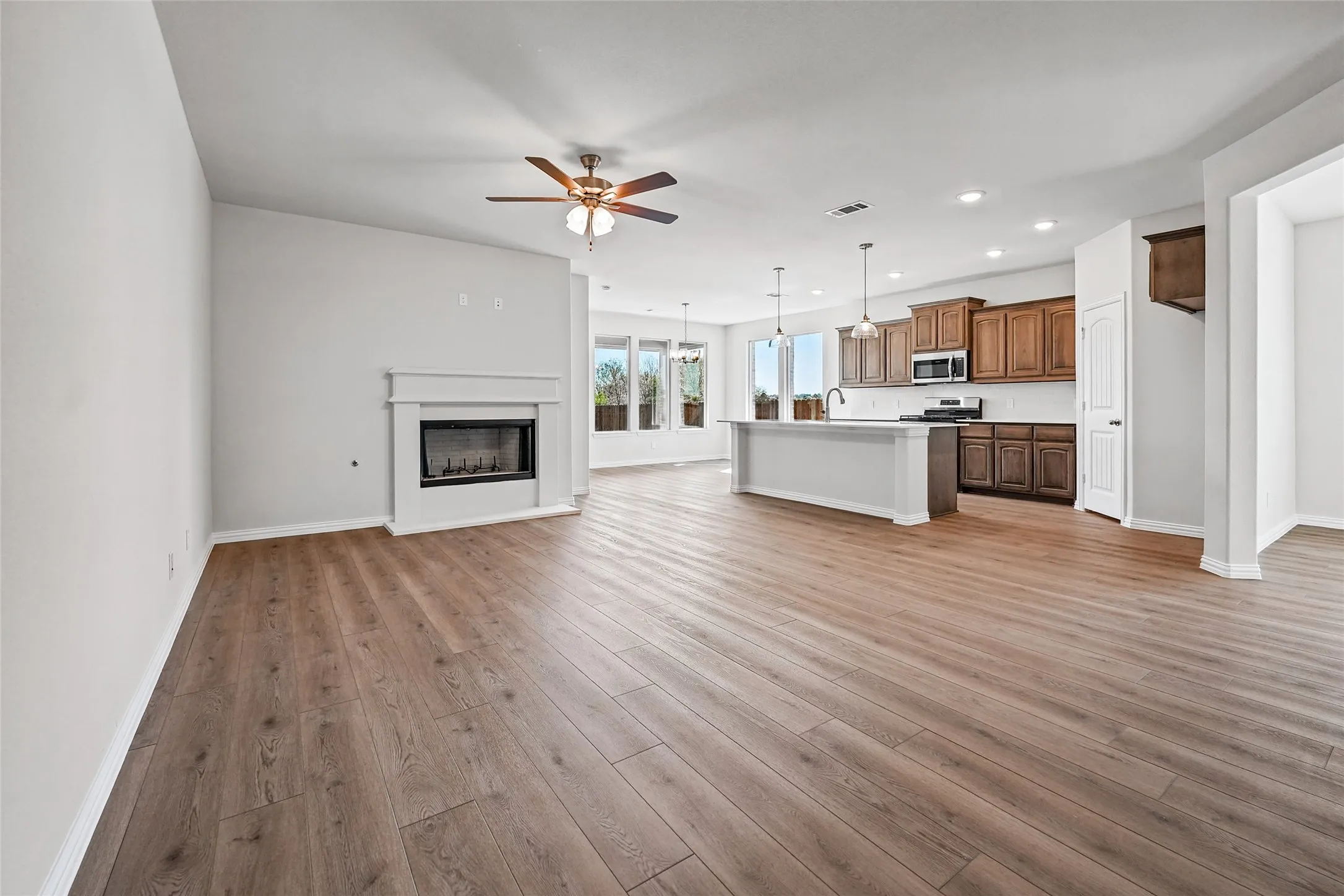 Wood-finish flooring throughout, with a built-in fireplace, a ceiling fan, recessed lighting, and a kitchen island with pendant lighting