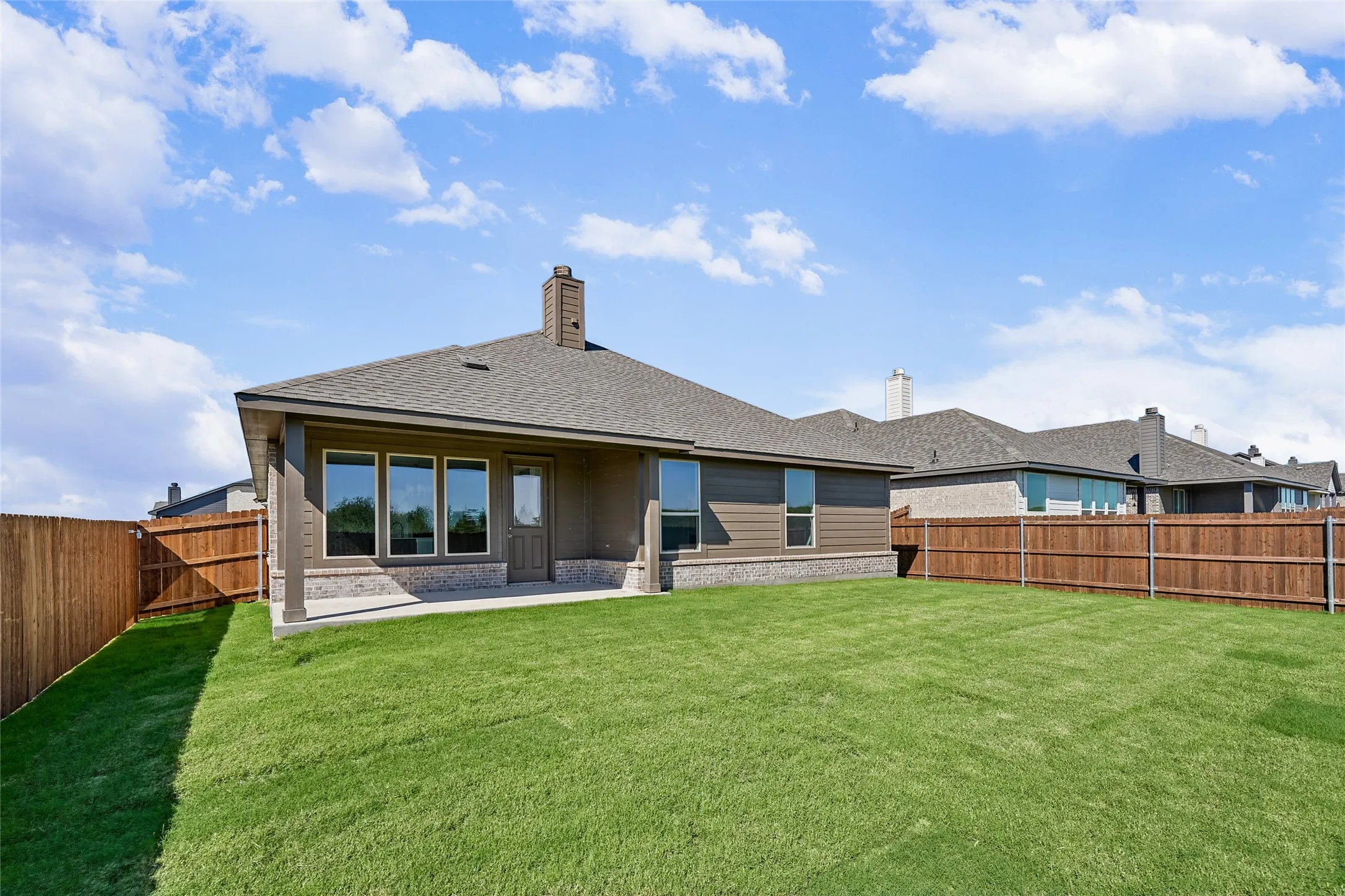 Expansive backyard with a manicured lawn, wood-paneled privacy fencing, and a covered concrete patio
