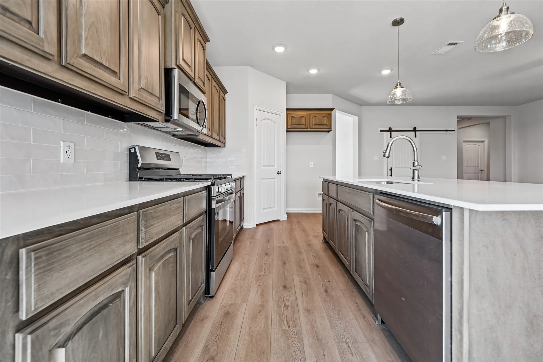 Kitchen featuring wood-finish cabinetry, stainless steel appliances, a white subway tile backsplash, and an island with a built-in sink and dishwasher