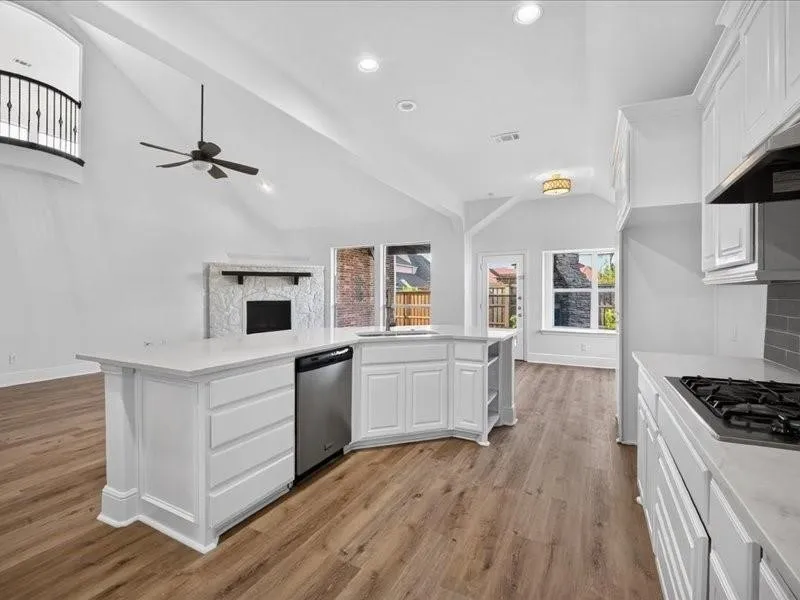 Open-concept kitchen and living area featuring wood-finish flooring, vaulted ceilings, and a fireplace with stone surround