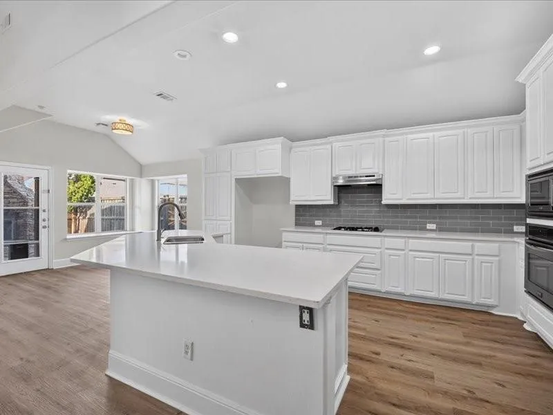 Open-concept kitchen featuring an island with a sink, white cabinetry, a gray subway tile backsplash, and wood-finish flooring