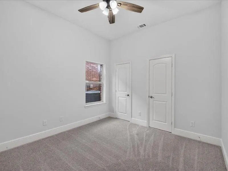 Neutral-toned carpet flooring, two paneled doors, and a ceiling fan with light fixture