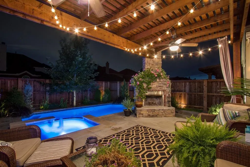 Covered patio featuring a wood beam ceiling with string lights, a stone fireplace, and a built-in outdoor ceiling fan