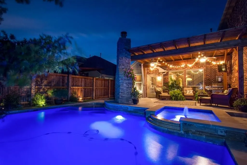 Inviting outdoor living space featuring a built-in swimming pool, integrated spa with water feature, brick exterior, wood pergola, and privacy fencing
