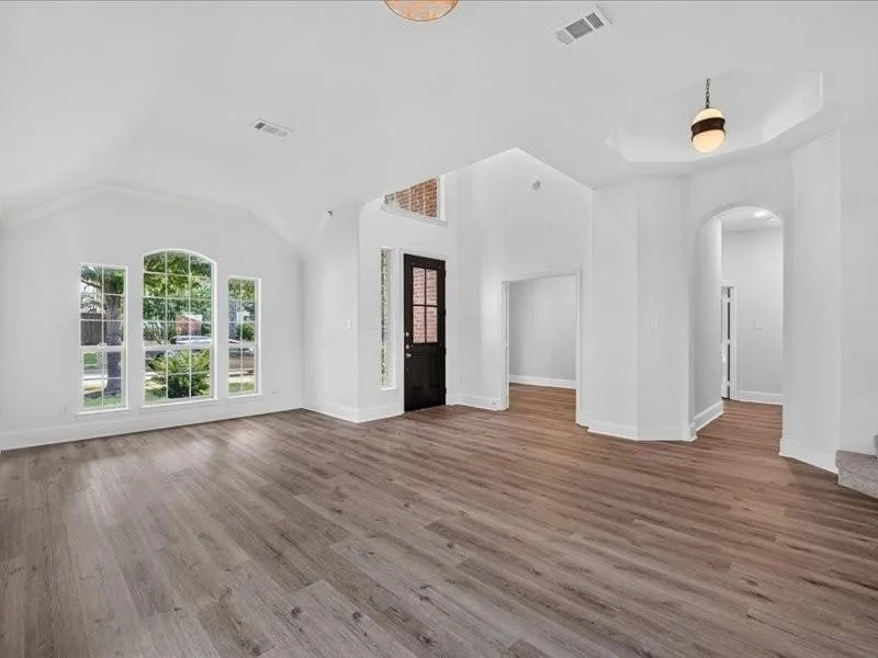 Vaulted ceiling, wood-finish flooring, arched windows, recessed lighting, and a tray ceiling