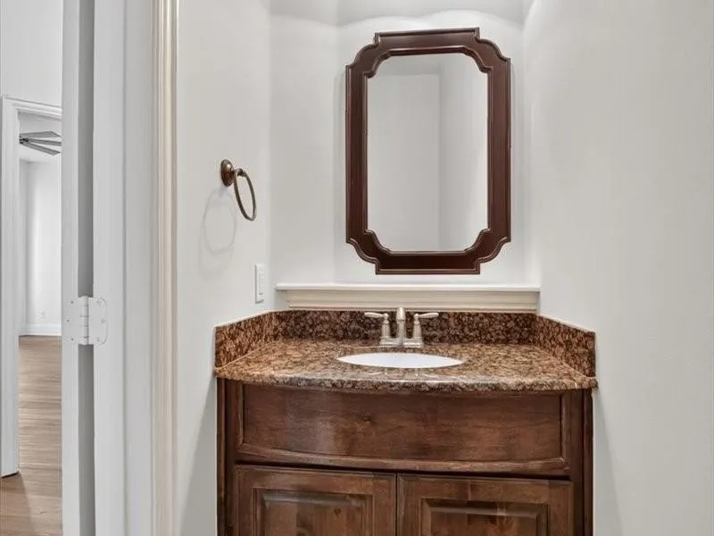 Wood-finish vanity with a built-in sink, stone-finish countertop, and decorative framed mirror