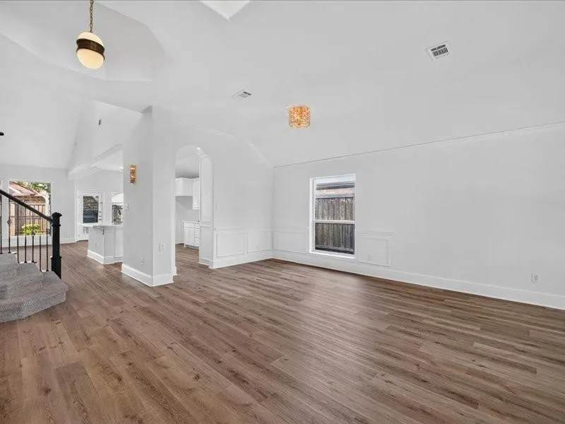 Wood-finish flooring, vaulted ceilings, wainscoting, arched doorway, and a contemporary light fixture