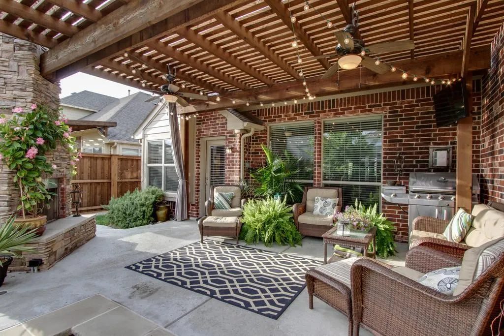 Expansive covered patio featuring a stone fireplace, wood pergola, multiple ceiling fans, and brick exterior